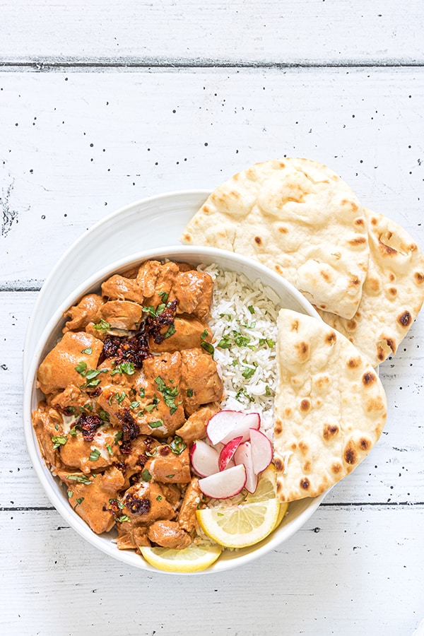 instant pot butter chicken in a white bowl with naan bread, diced radishes, and sliced lemons