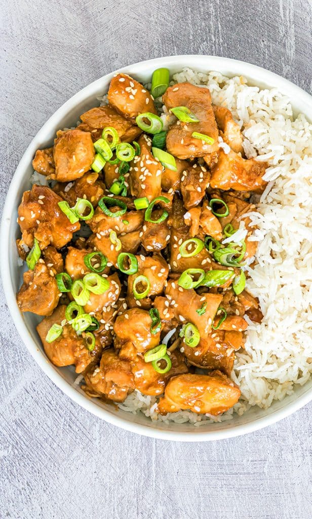 instant pot sesame chicken in a white bowl with white rice and green onions sliced on top