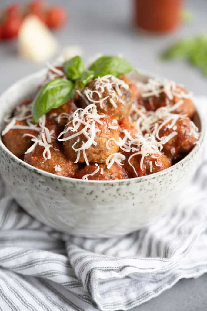 fresh baked keto meatballs in a bowl with fresh basil and shredded mozzarella