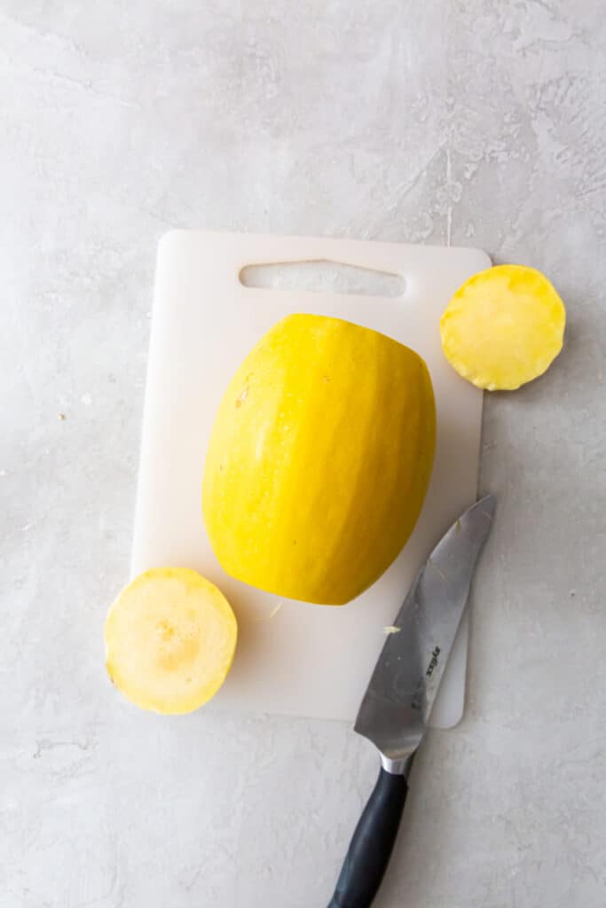 whole spaghetti squash on a white cutting board with top and bottom cut off