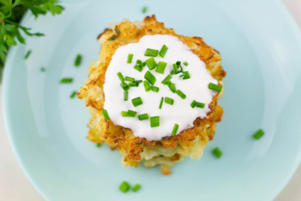 overhead shot of pan seared cauliflower fritters on a blue plate topped with sour cream and diced green onions