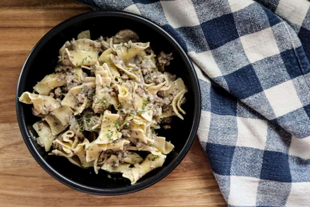ground beef stroganoff in a black bowl with a blue and white checkered napkin