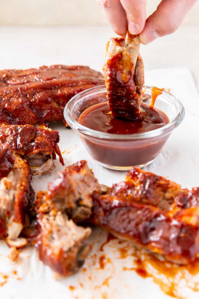 baby back rib being dunked in a bowl of bbq sauce
