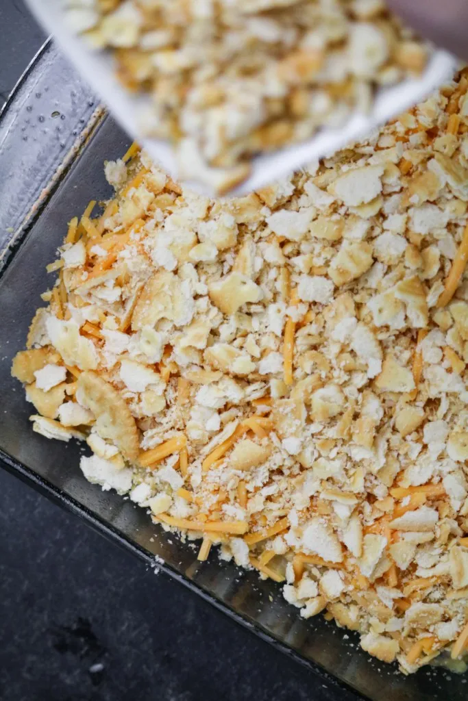 crackers being placed on top of the southern squash casserole in a glass dish