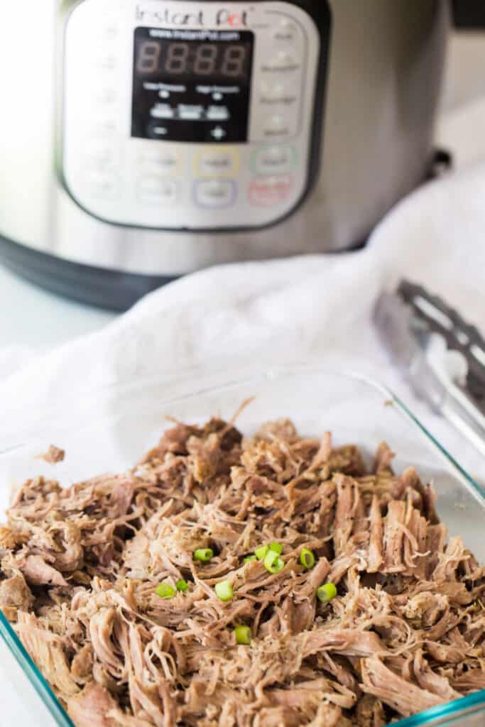 pulled pork in a glass dish in front of an instant pot pressure cooker