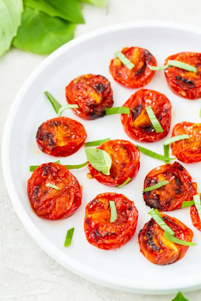 air fryer roasted tomatoes on a white plate and green basil