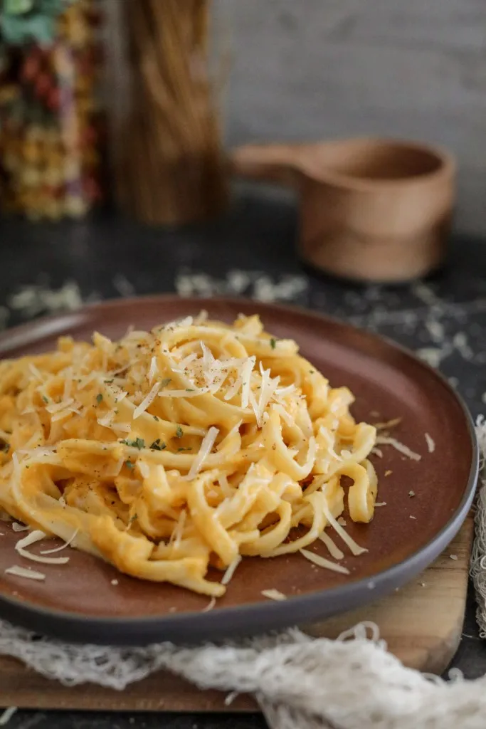 fettuccine butternut squash alfredo on a brown plate with parmesan grated on top