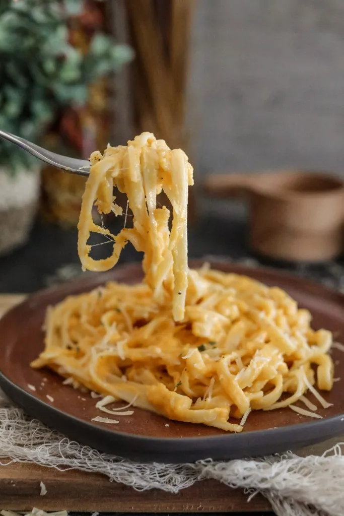 side view of fettuccine butternut squash alfredo pasta recipe on a fork and brown plate