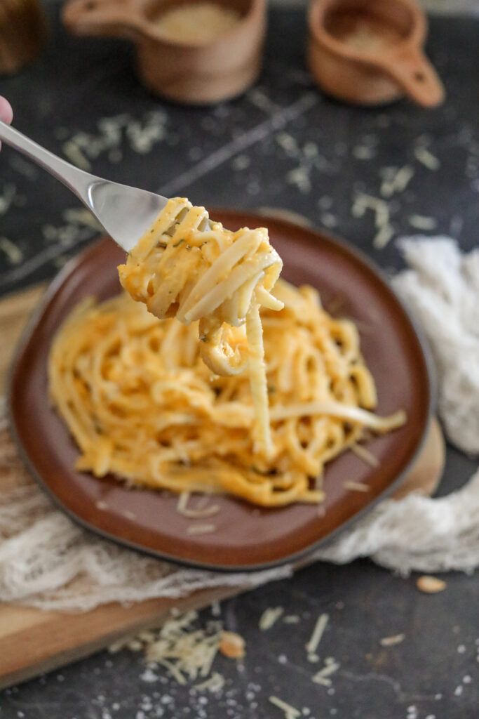 fettuccine butternut squash alfredo on a fork in front of a brown plate