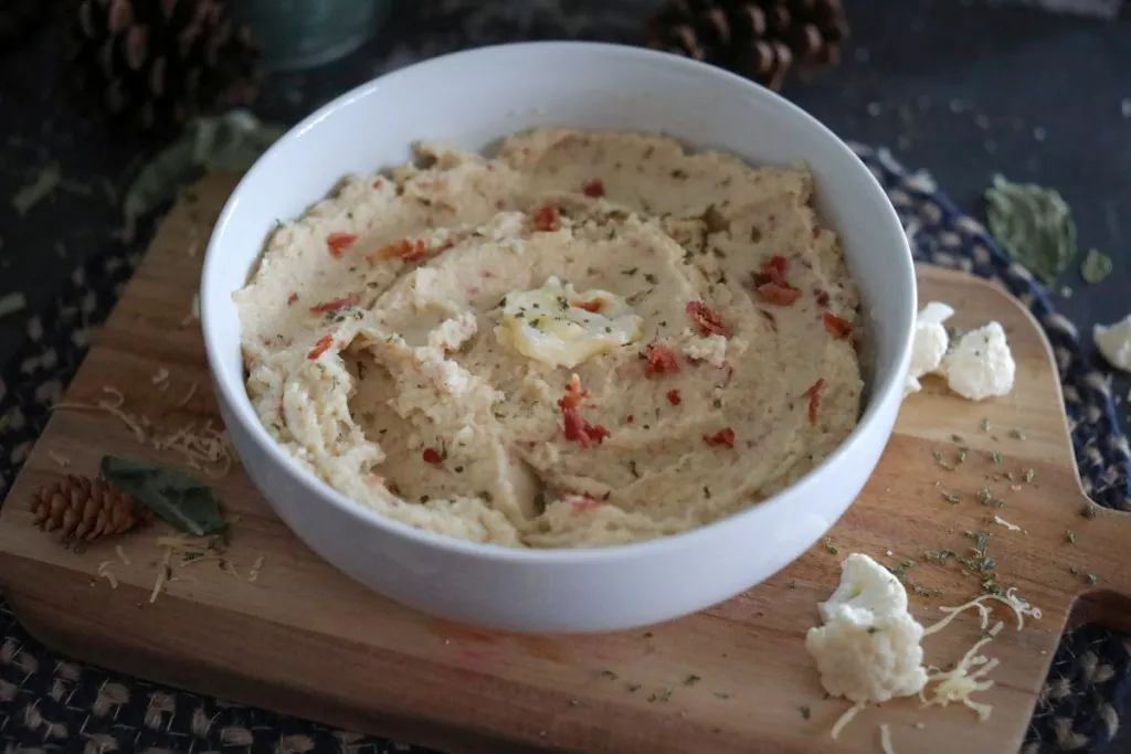 a white bowl of cauliflower mash with bacon bits on top