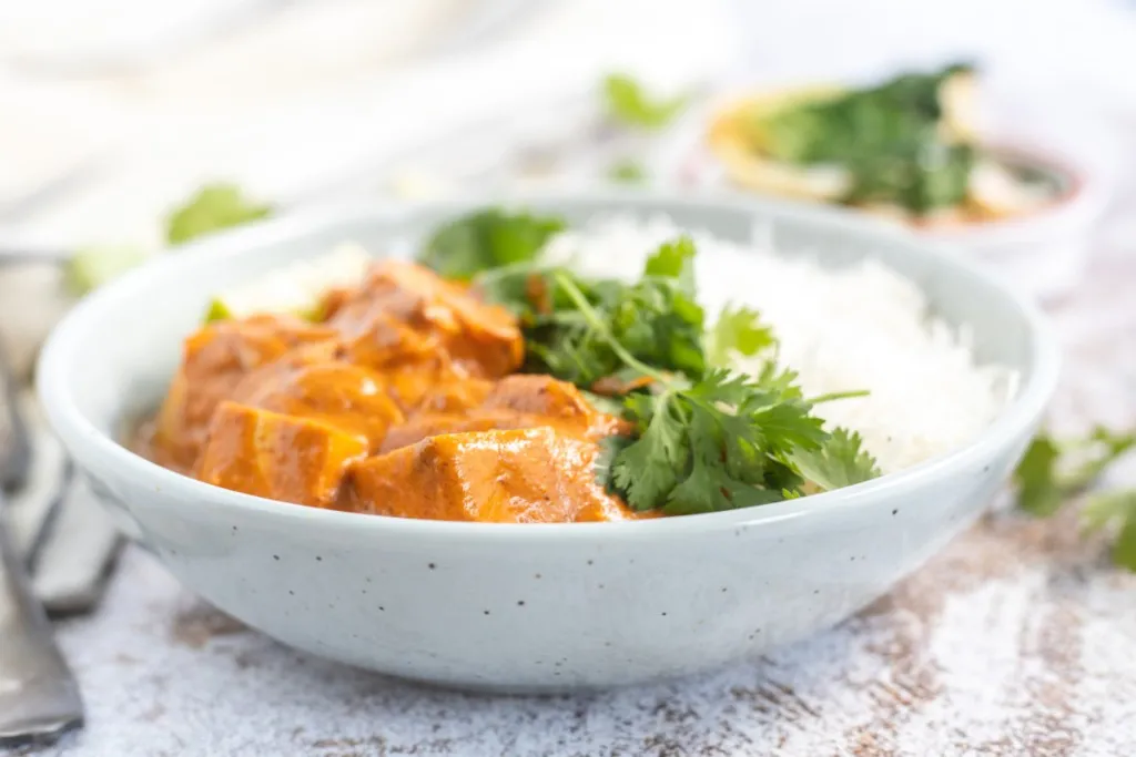 side view of instant pot tofu curry in a white bowl with a side of rice