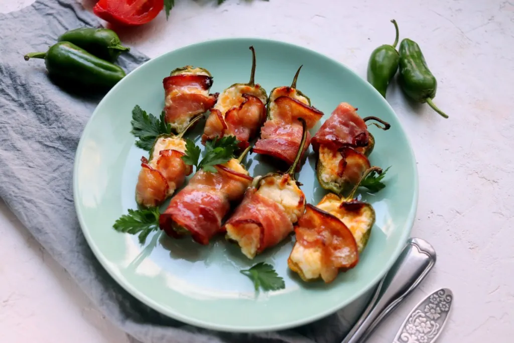 overhead shot of keto bacon wrapped jalapenos on a blue plate with parsley