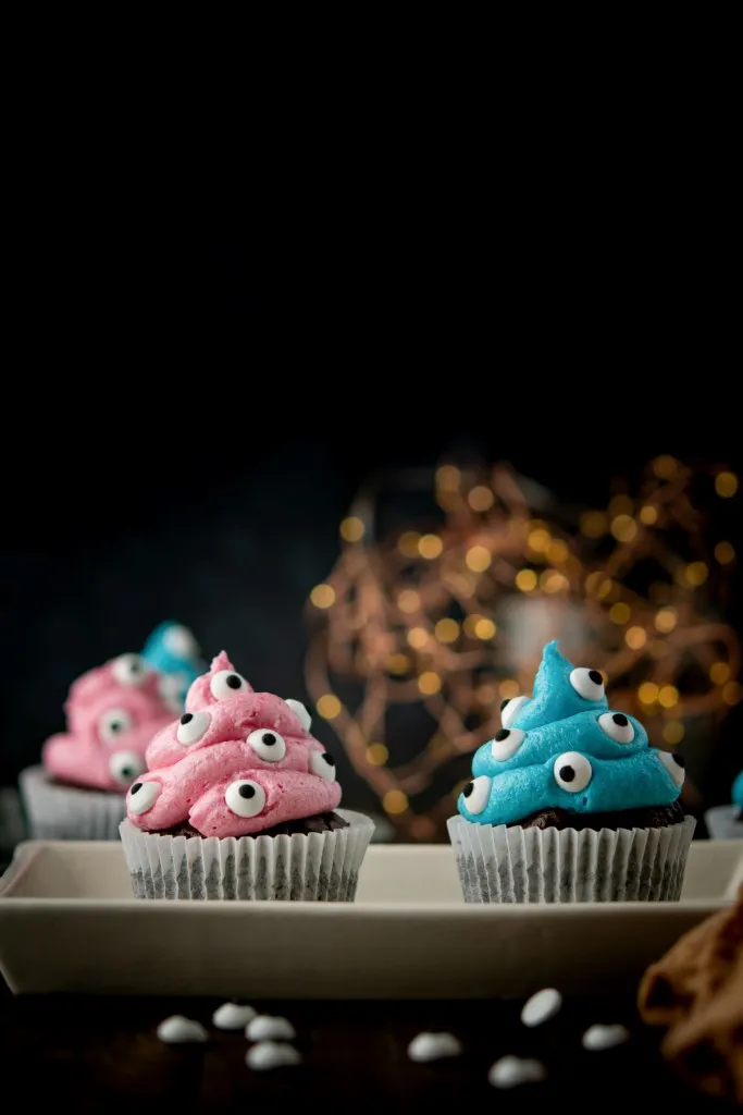 blue and pink monster cupcakes in white cupcake liners with light in back