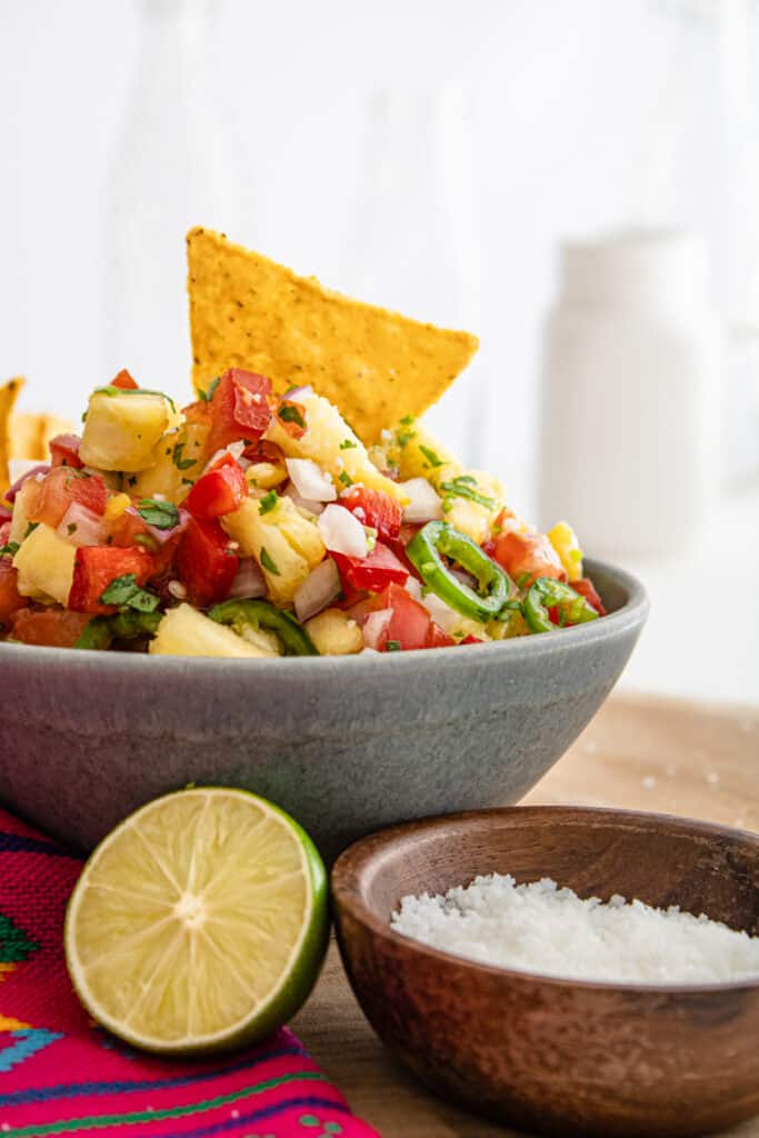 close up side view pineapple salsa in a gray bowl with a chip in it
