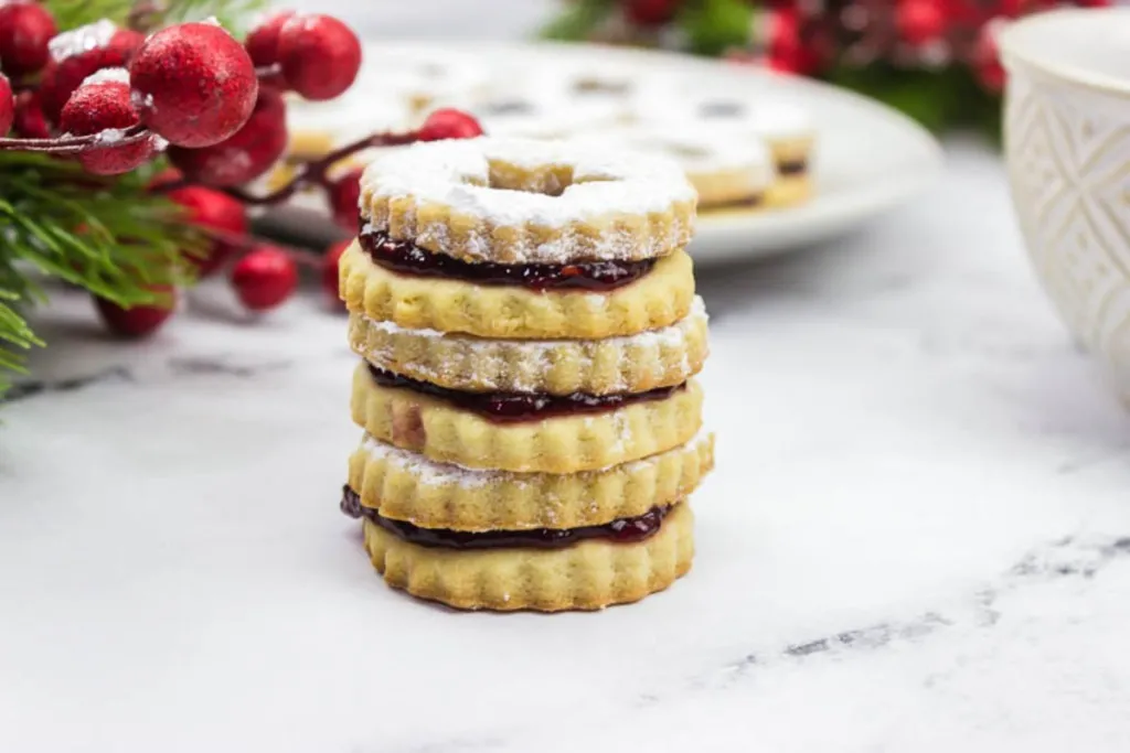 side shot of christmas linzer ookies with cranberries and pine in the background