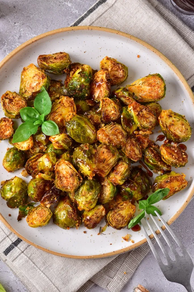 air fryer brussels sprouts with a balsamic drizzle and grated parmesan garnished with fresh basil on a stone colored plate