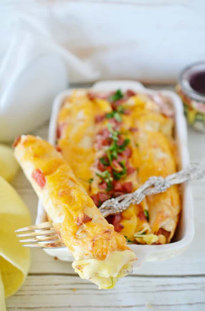 overhead shot of a breakfast enchilada on a fork on a casserole white dish with crumbled bacon on top