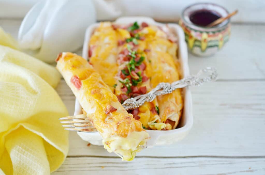 breakfast enchiladas in a white baking casserole dish with a fork and yellow napkin on the side