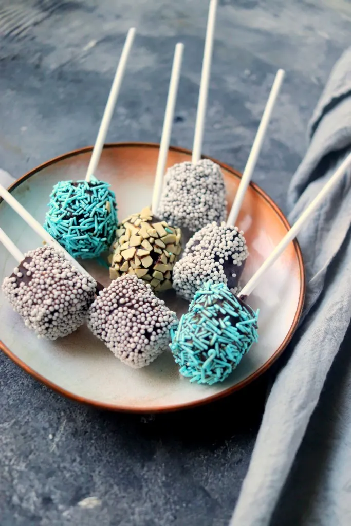 chocolate covered marshmallows on sticks on a plate and grey background
