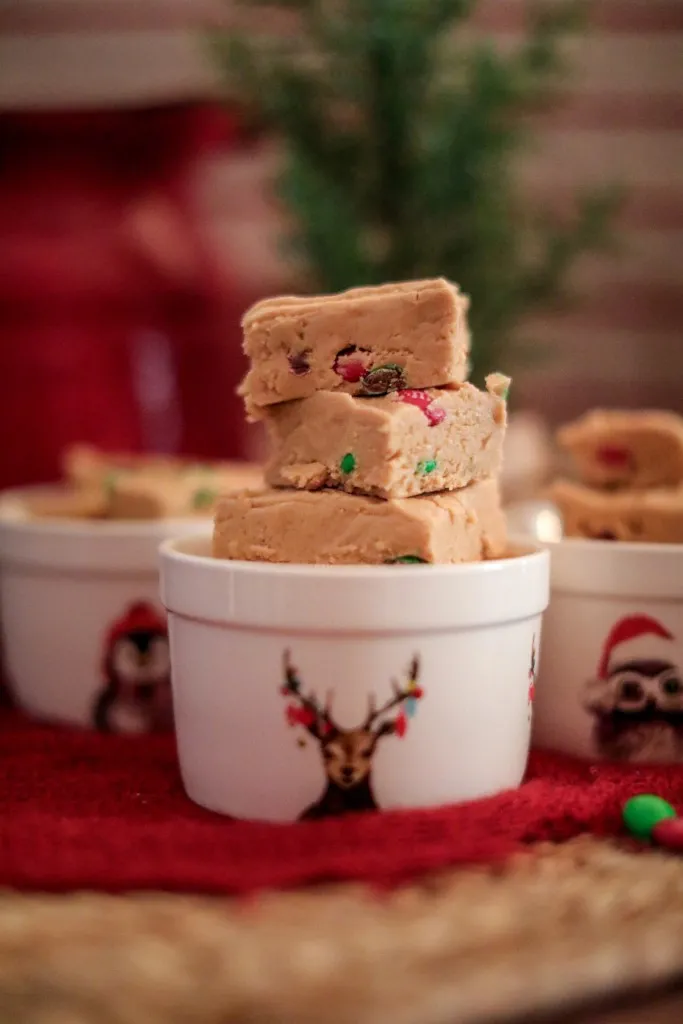 christmas peanut butter fudge with red and green m&ms in white ceramic christmas dishes