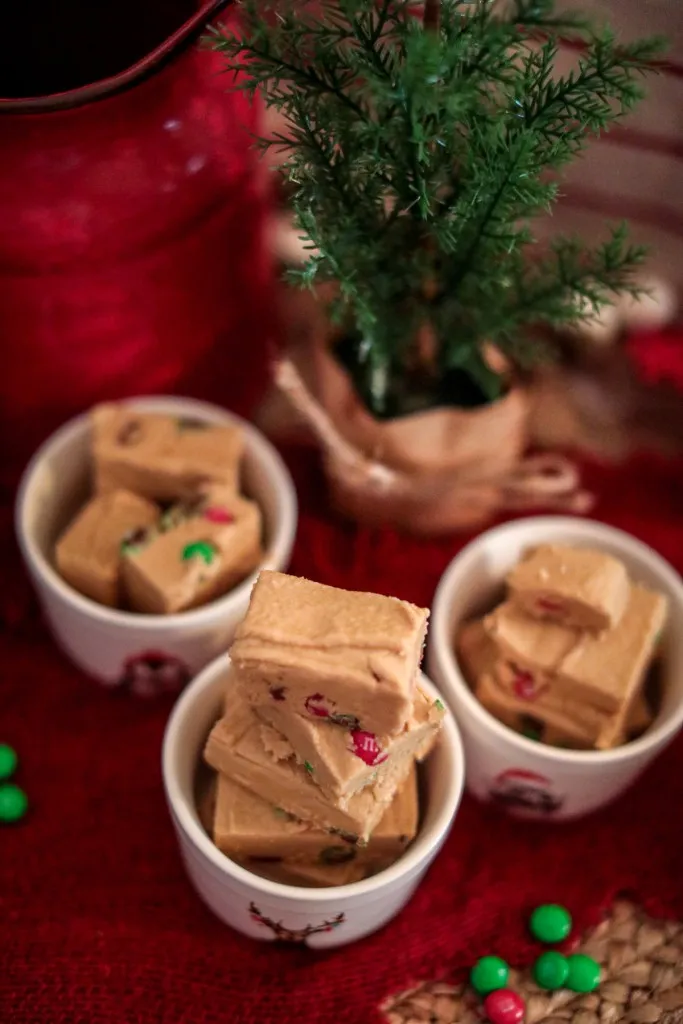 3 white christmas decorated bowls filled with holiday peanut butter fudge on a red background