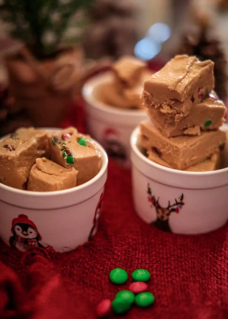 a trail of red and green m&ms that lead to peanut butter fudge in festive decorated white dishes