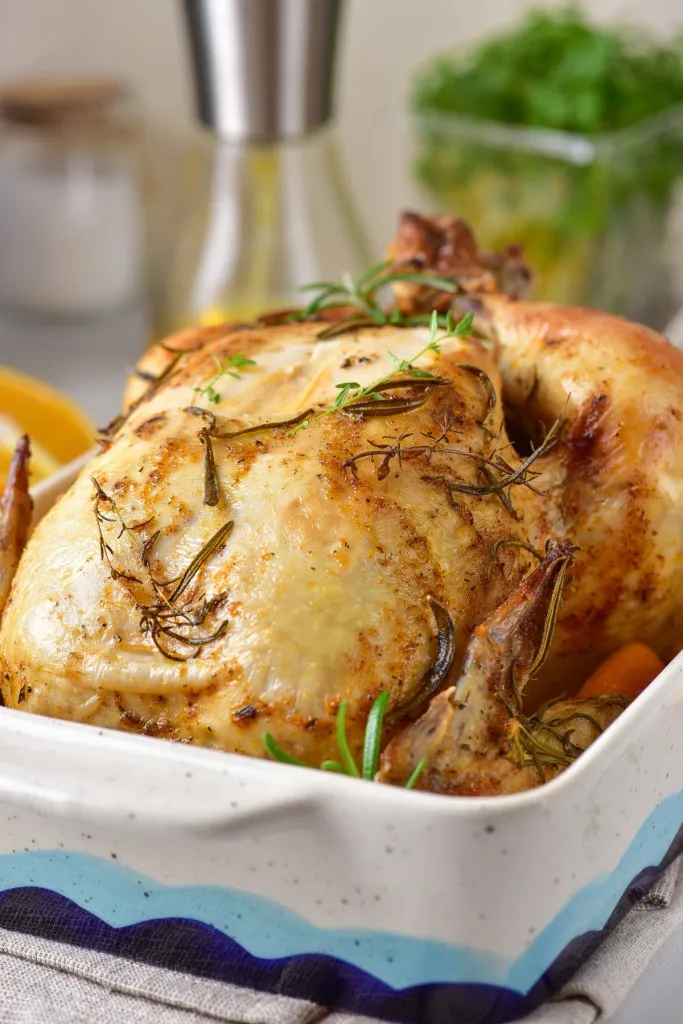 close up view of orange roasted chicken with fresh herbs