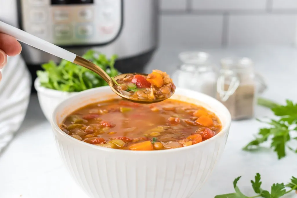 a sideview of Instant Pot lentil soup with a spoon and white bowl
