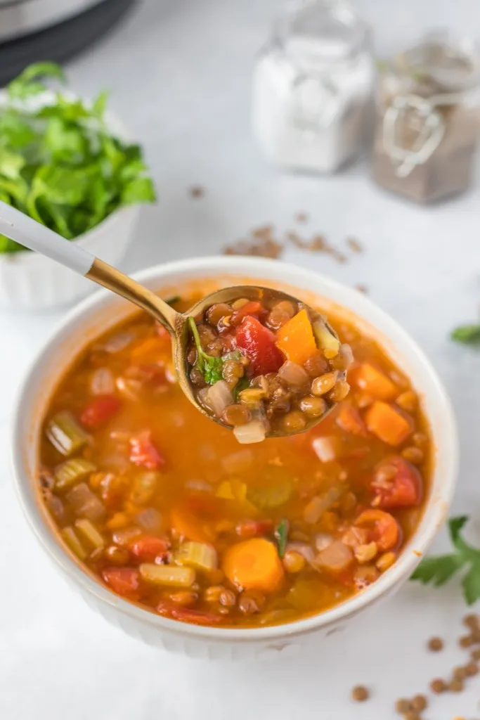 gold and white soup spoon filled with lentil soup hovering over a bowl of lentil soup in a white bowl
