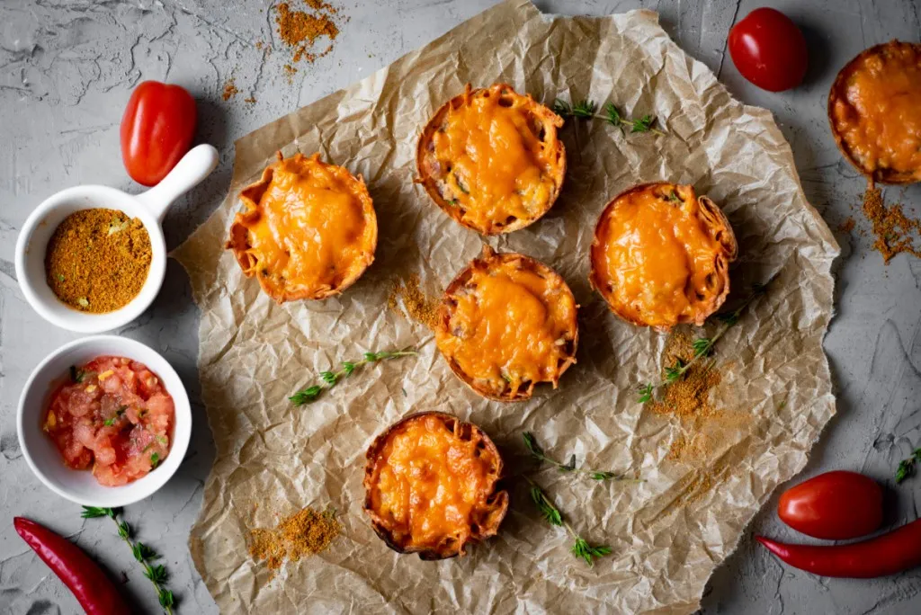 overhead view mini mexican pizzas on parchment paper with a bowl of salsa with red peppers and tomatoes in background