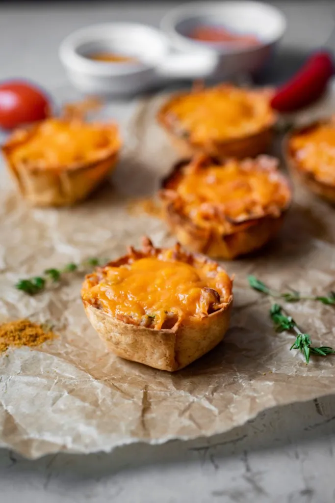 a few mini mexican pizzas on parchment paper with a bowl of salsa with red peppers and tomatoes in background