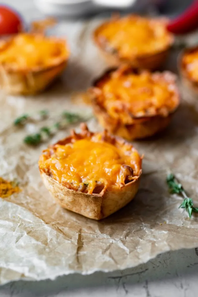 close up shot of mini mexican pizzas on parchment paper with a bowl of salsa with red peppers and tomatoes in background with fresh herbs