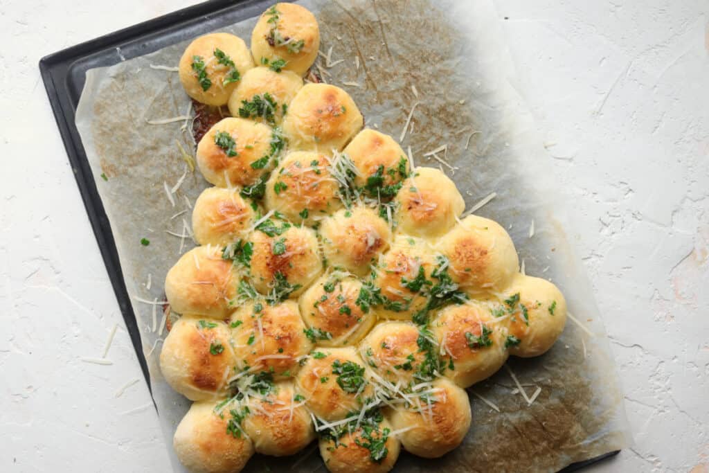 overhead shot of pull apart christmas rolls topped with fresh herbs and parmesan cheese
