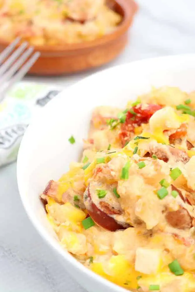 close up view of slow cooker cheesy potatoes with diced chives to garnish in a white bowl