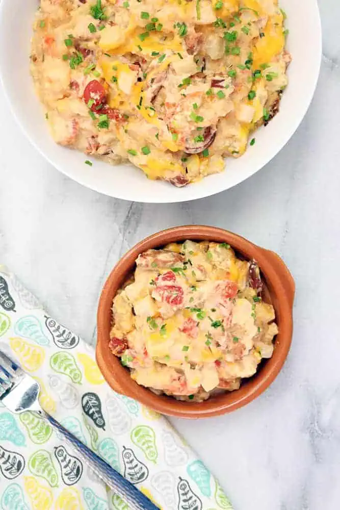 cheesy potatoes made in a slow cooker served in a white dish and small brown bowl