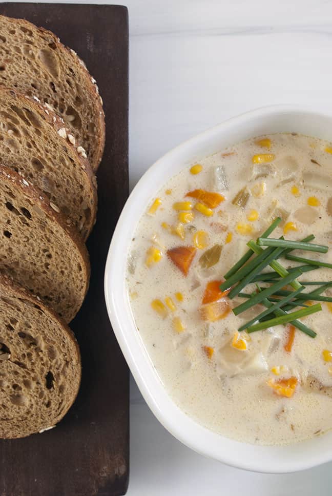 sliced wheat bread next to corn chowder in a white bowl