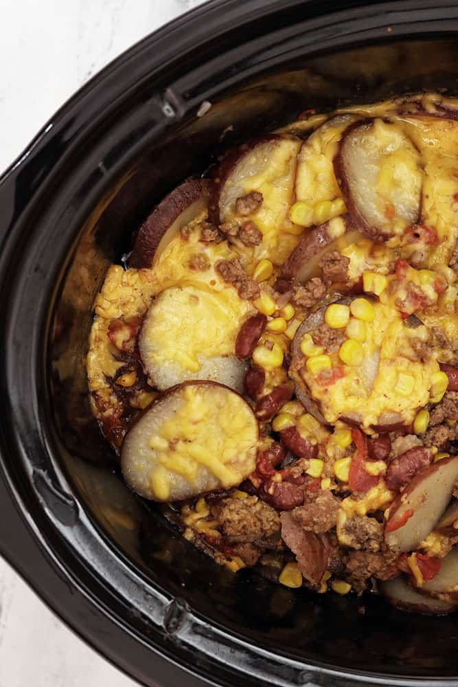 slow cooker cowboy potatoes in a black crockpot topped with melted cheddar cheese
