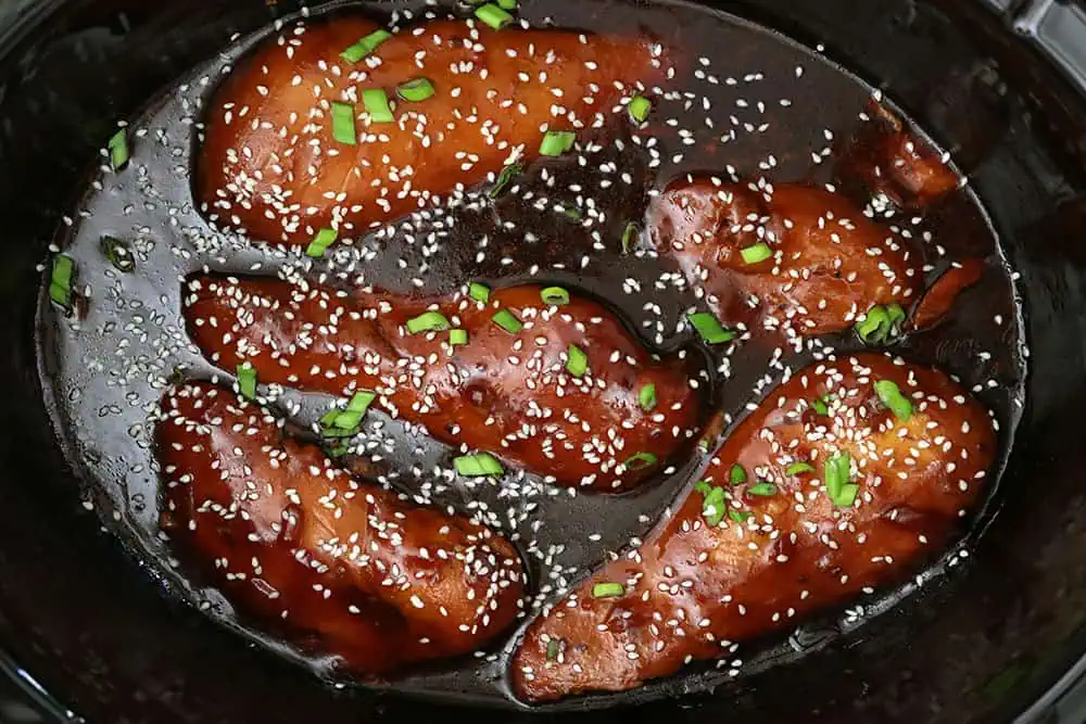 sesame chicken in a slow cooker sprinkled with green onions and sesame seeds