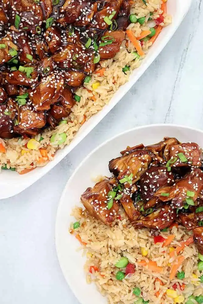 overhead shot of slow cooker sesame chicken served on a white plate with sesame seeds and diced green onions