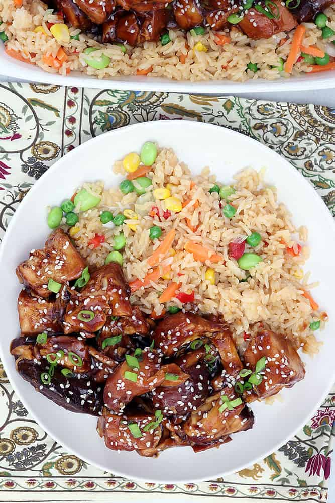 side by side sesame chicken with friend rice on a decorated linen with hints of greens and red