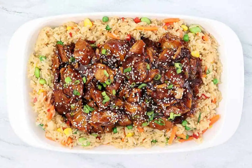 sesame chicken over a bed of vegetable fried rice on a white plate