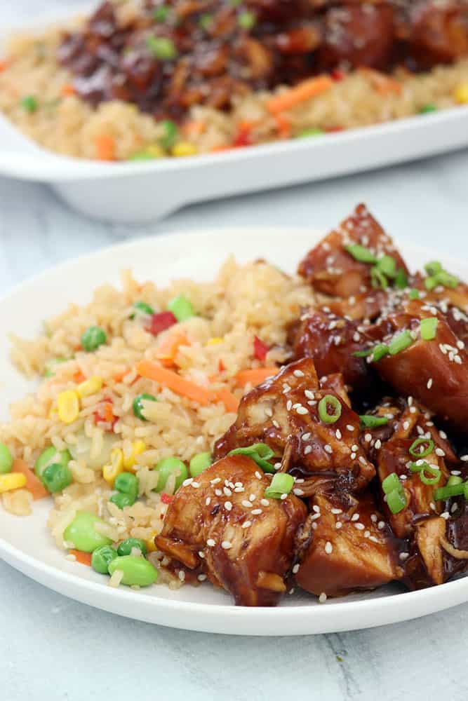 side view of crockpot sesame chicken on a white plate with vegetable fried rice
