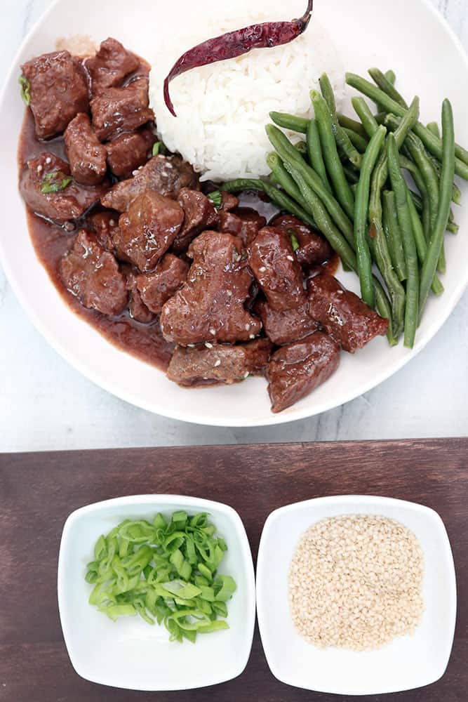 slow cooker korean beef on a white plate with rice and sesame seeds