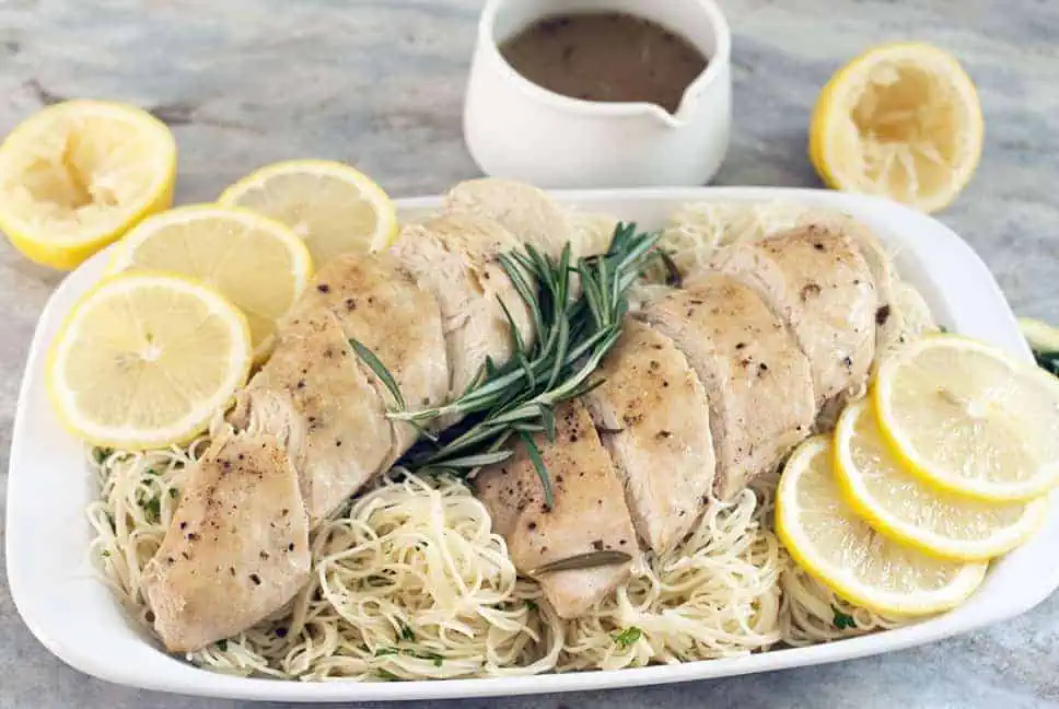 over head shot of sliced slow cooker lemon chicken with fresh herbs, lemons, and angel hair pasta