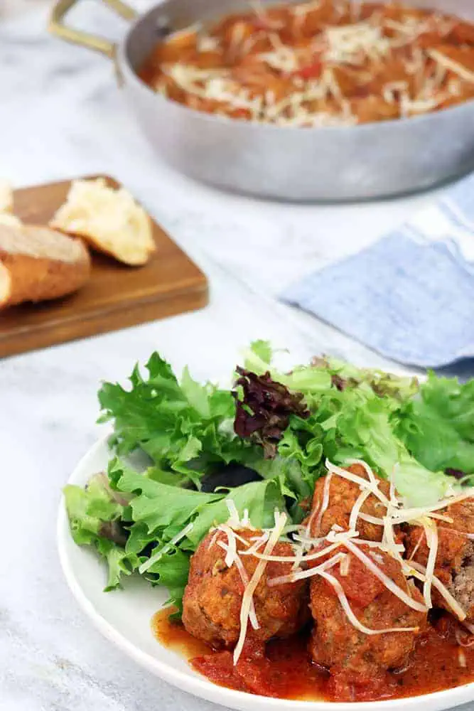 hero shot of slow cooker meatballs and mixed greens salad on a white plate in front of a dark wooden board with bread