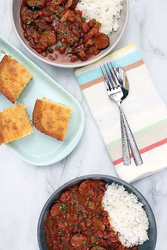 2 bowls of red beans and rice with a plate of corn bread in the middle