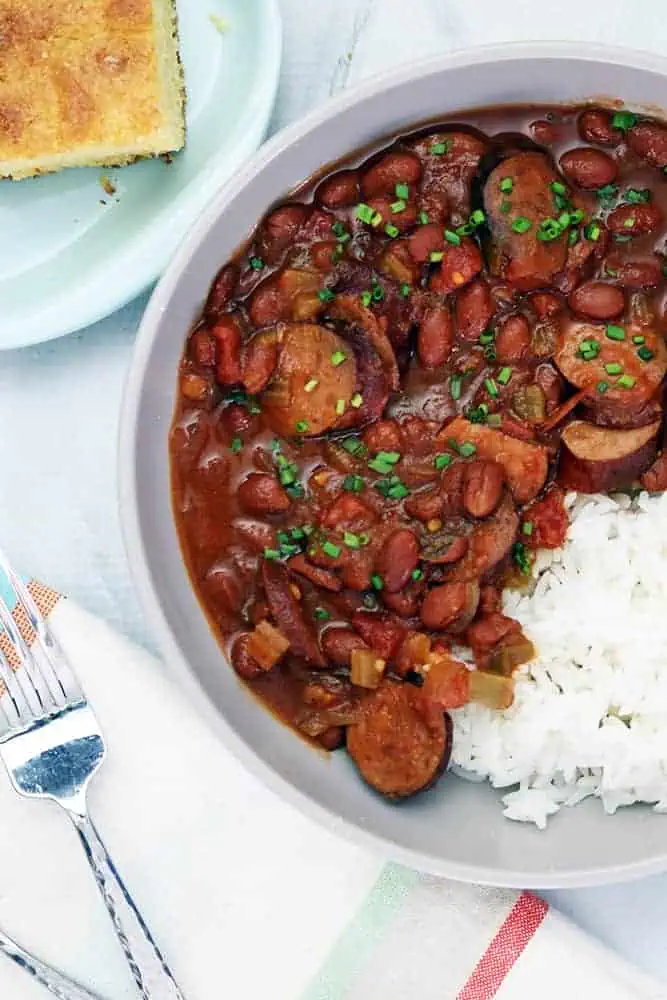 a bowl of red beans and rice made in a crock pot next to a plate of corn bread