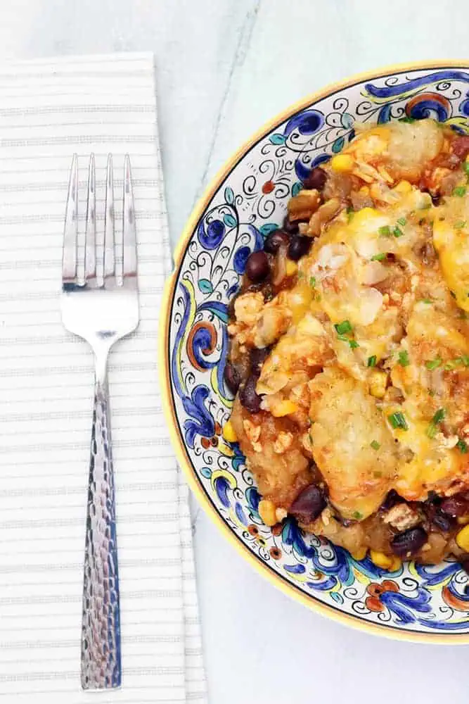 blue and orange flat bowl with slow cooker tater tot casserole with a fork next to it