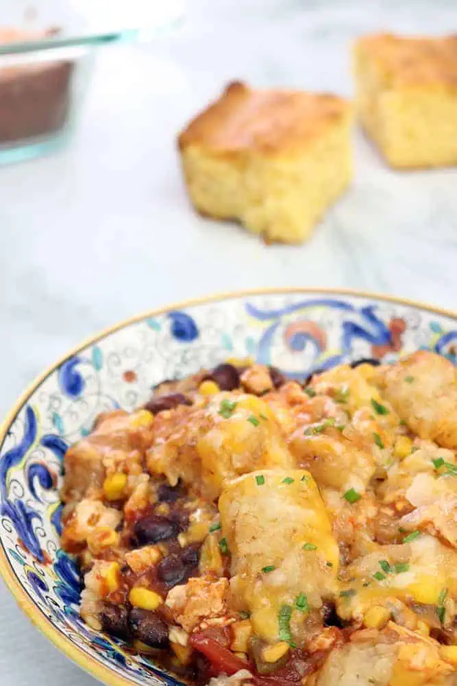 close up view of slow cooker tater tot casserole in a flat blue designed bowl with corn bread in the background