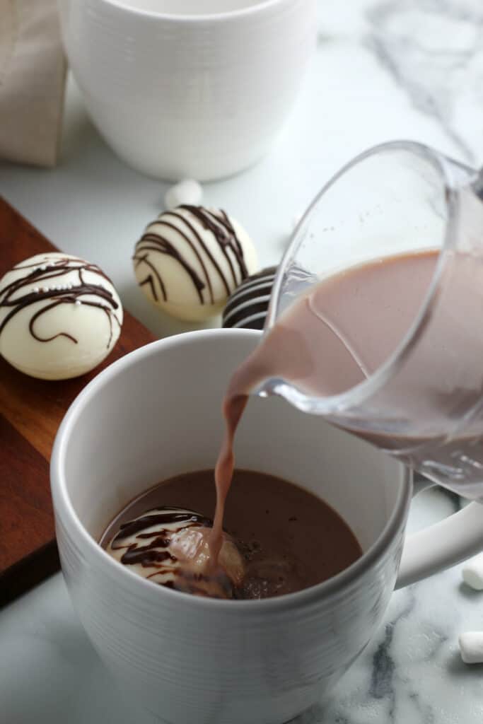 Chocolate milk being poured into a cup with a hot chocolate bomb in it